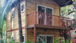 A wooden house with a balcony, surrounded by lush greenery and flowering plants. - Mariners Bay Resorts (Mandrem)