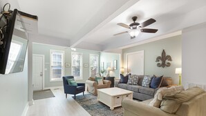 A spacious living room with a ceiling fan, a large window, and a door leading to another room. - Salty Shack #B - Across from the Beach - Central Location (Folly Beach)