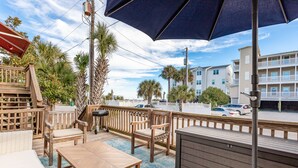 A wooden deck with outdoor furniture, including a table and chairs, and a large umbrella providing shade. - Salty Shack #B - Across from the Beach - Central Location (Folly Beach)