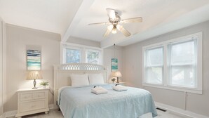 A bedroom with a bed, nightstands, a ceiling fan, and large windows. - Salty Shack #B - Across from the Beach - Central Location (Folly Beach)