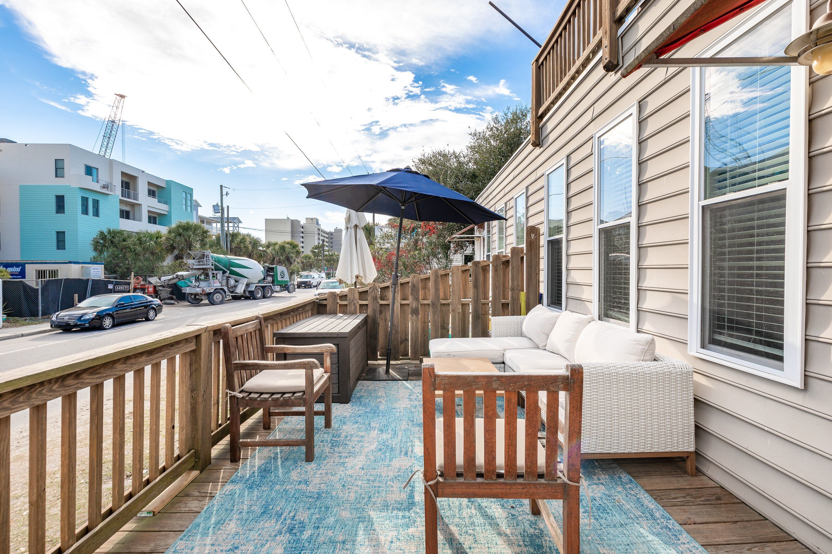 A wooden deck with outdoor furniture, a blue rug, and a large umbrella.