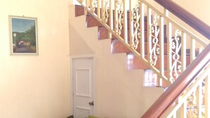 A staircase with ornate balusters, a red sofa with green cushions, and a door in the background.