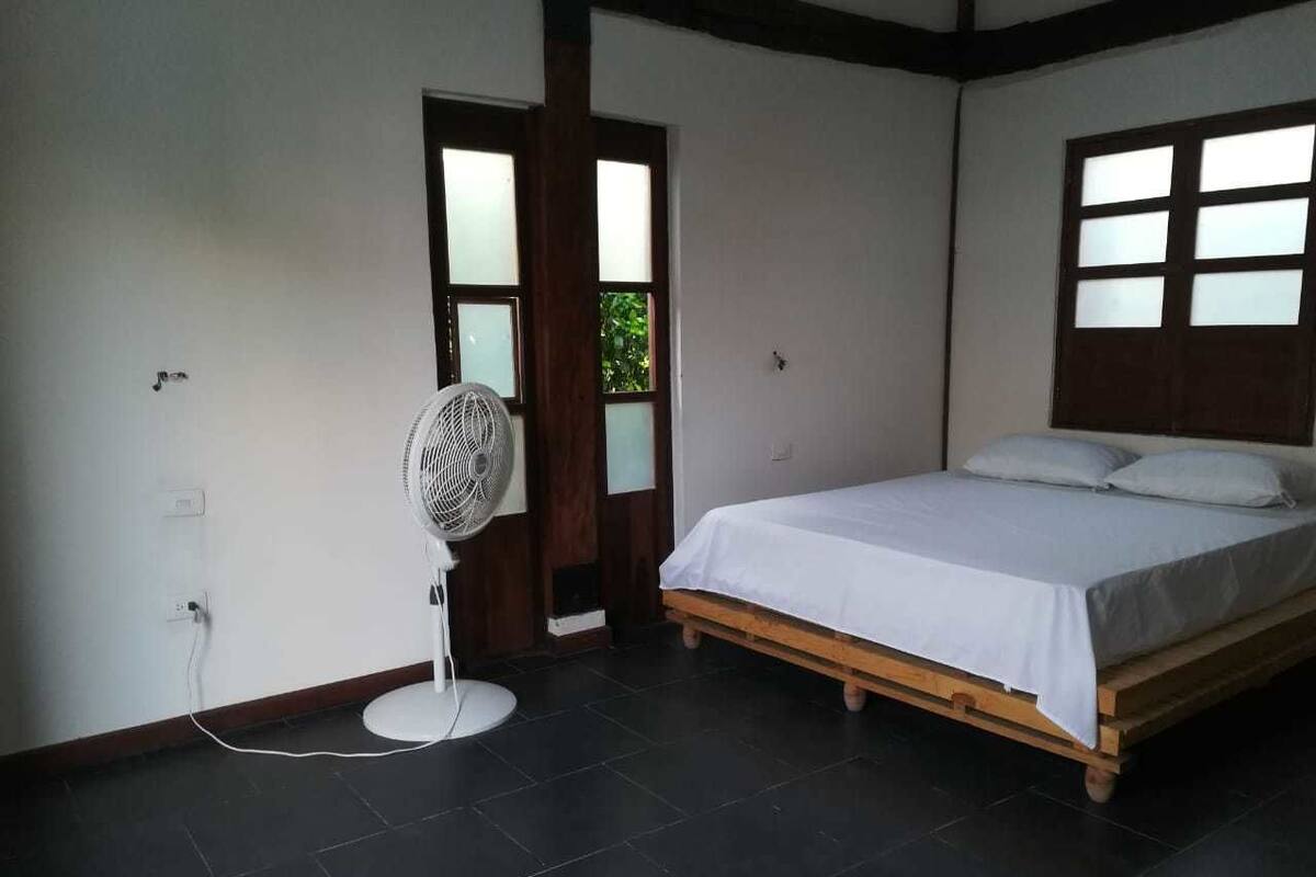 Ein Schlafzimmer mit einem Bett, einem Standventilator und einer Tür, die nach draußen führt.
