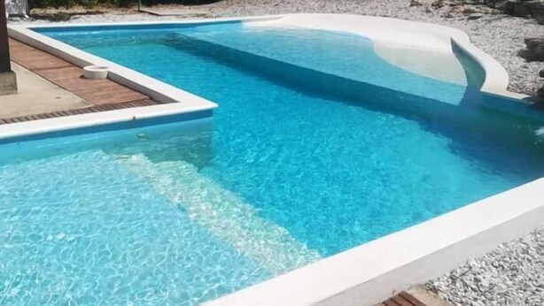 Una piscina rectangular con agua azul cristalina, rodeada por una terraza de madera y una zona junto a la piscina en blanco.