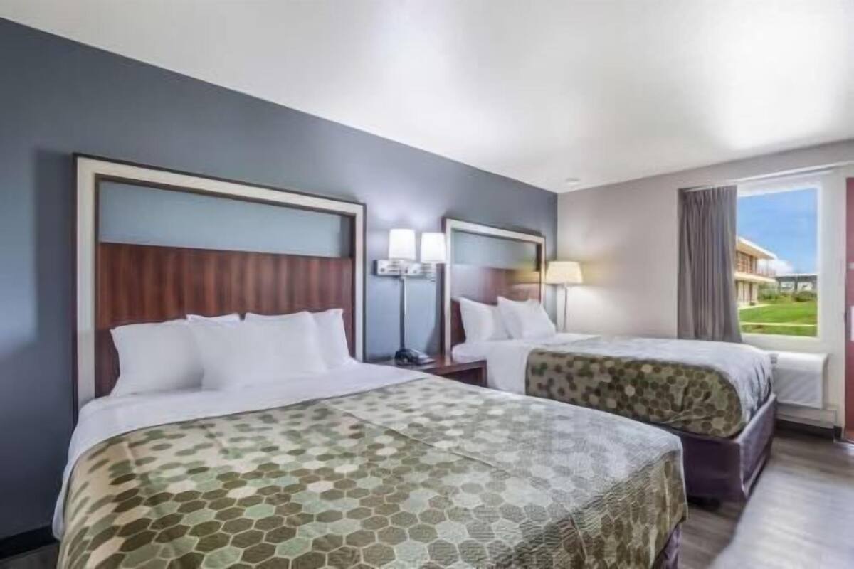 A hotel room with two beds, a large window, and a view of a building outside.