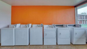A laundry room with four front-loading washing machines against an orange wall, with a large window on the right. - Econo Lodge Neenah (Neenah)