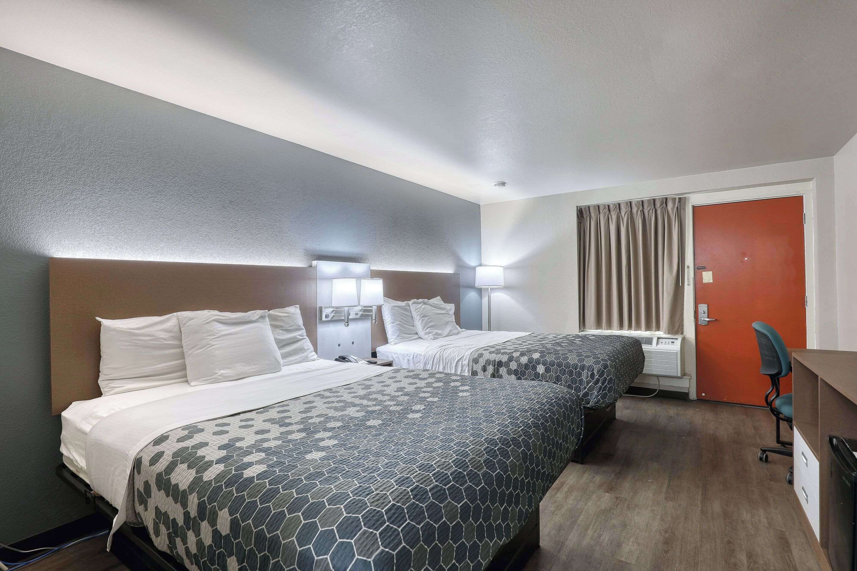 A hotel room with two beds, a desk, and a chair.