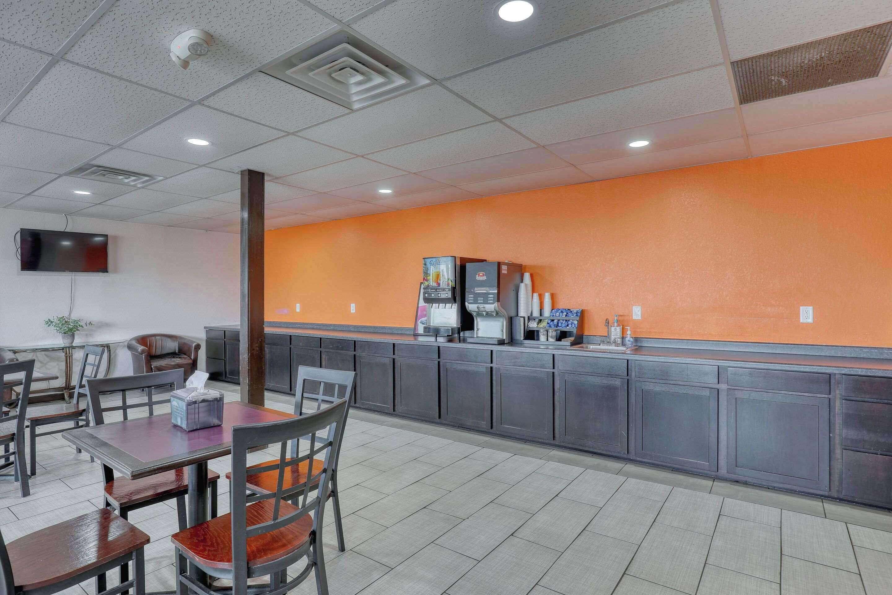 A restaurant with a counter, chairs, tables, and a television on the wall.