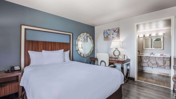 A hotel room with a large bed, a desk with a lamp, a mirror, and a bathroom with a sink and mirror. - Econo Lodge Neenah (Neenah)