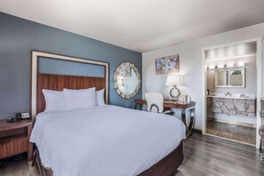 A hotel room with a large bed, a desk with a lamp, a mirror, and a bathroom with a sink and mirror. - Econo Lodge Neenah (Neenah)