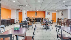 A dining area with tables and chairs, an exit sign, and a kitchen counter. - Econo Lodge Neenah (Neenah)