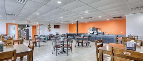 Un comedor interior amplio con varias mesas y sillas de madera, una encimera de cocina y suelo de baldosas.