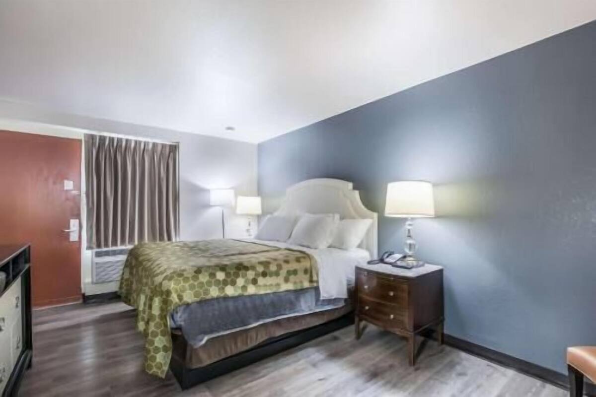 A hotel room with a bed, bedside lamps, a dresser, and a window with curtains.