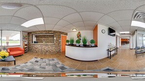 A reception area with a stone wall, orange sofas, a coffee table with flowers, and a TV on the wall. - Econo Lodge Neenah (Neenah)