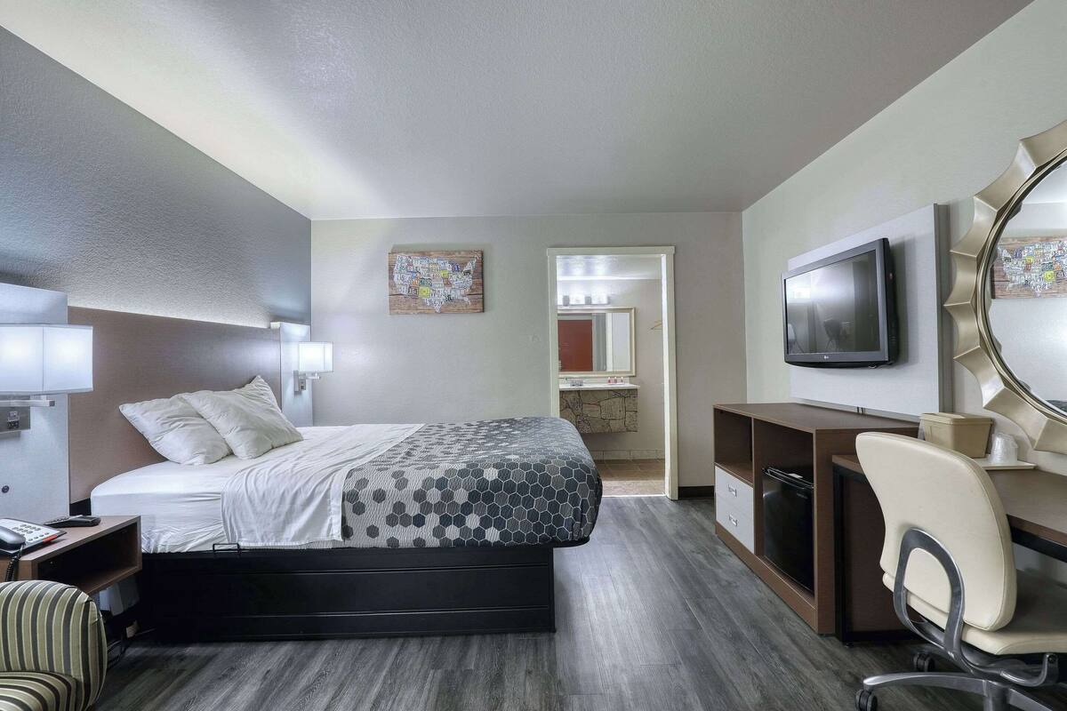 A hotel room with a bed, desk, chair, TV, and a bathroom visible through an open door.
