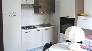 A compact kitchen with white cabinets, a gas stove, a sink, and a microwave. - Apartment close to the beach (Alghero)