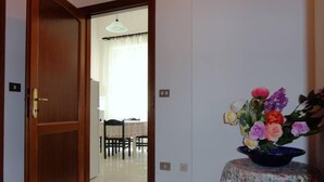 A room with a wooden door, a tiled floor, a table with chairs, and a floral tablecloth. - Apartment close to the beach (Alghero)