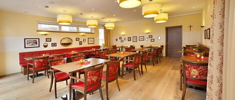 Een restaurant met houten tafels en rode, beklede zitbanken, met hanglampen en ingelijste foto's aan de muur.