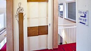 An elevator with a wooden panel design, a red carpeted floor, and a wall-mounted sign indicating time slots. - Hotel Greinwald (Marktoberdorf)