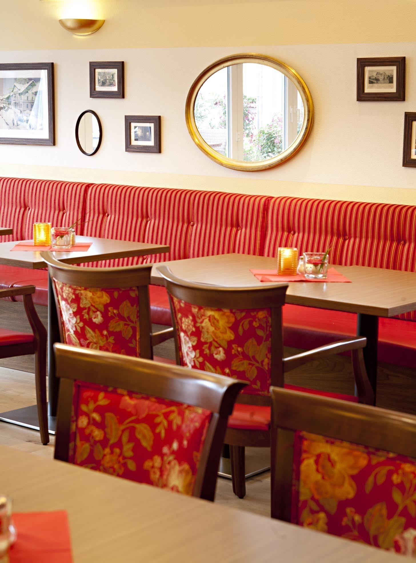 Interior de restaurante con asientos tipo cabina a rayas rojas, mesas de madera y sillas con estampado floral.