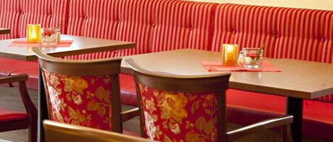 Interior de restaurante con asientos tipo cabina a rayas rojas, mesas de madera y sillas con estampado floral.