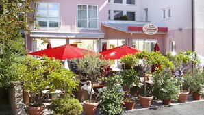 A hotel with outdoor seating, potted plants, and a sign indicating it is a cafe and hotel. - Hotel Greinwald (Marktoberdorf)