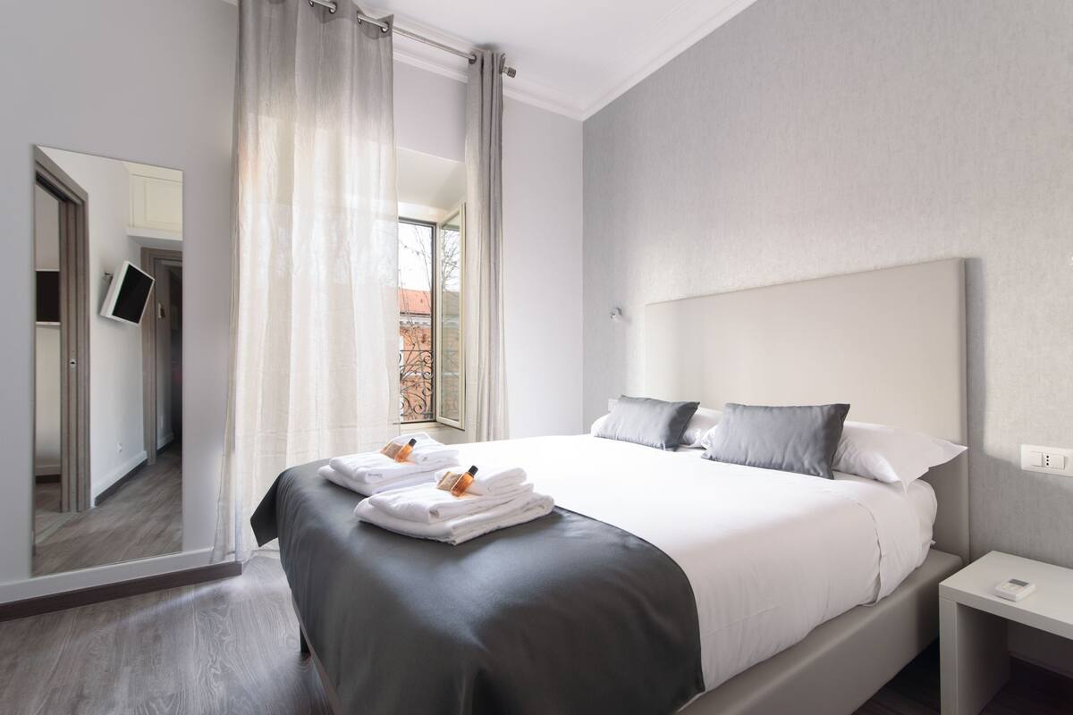A modern hotel room with a large bed, a bedside table, and a mirror.
