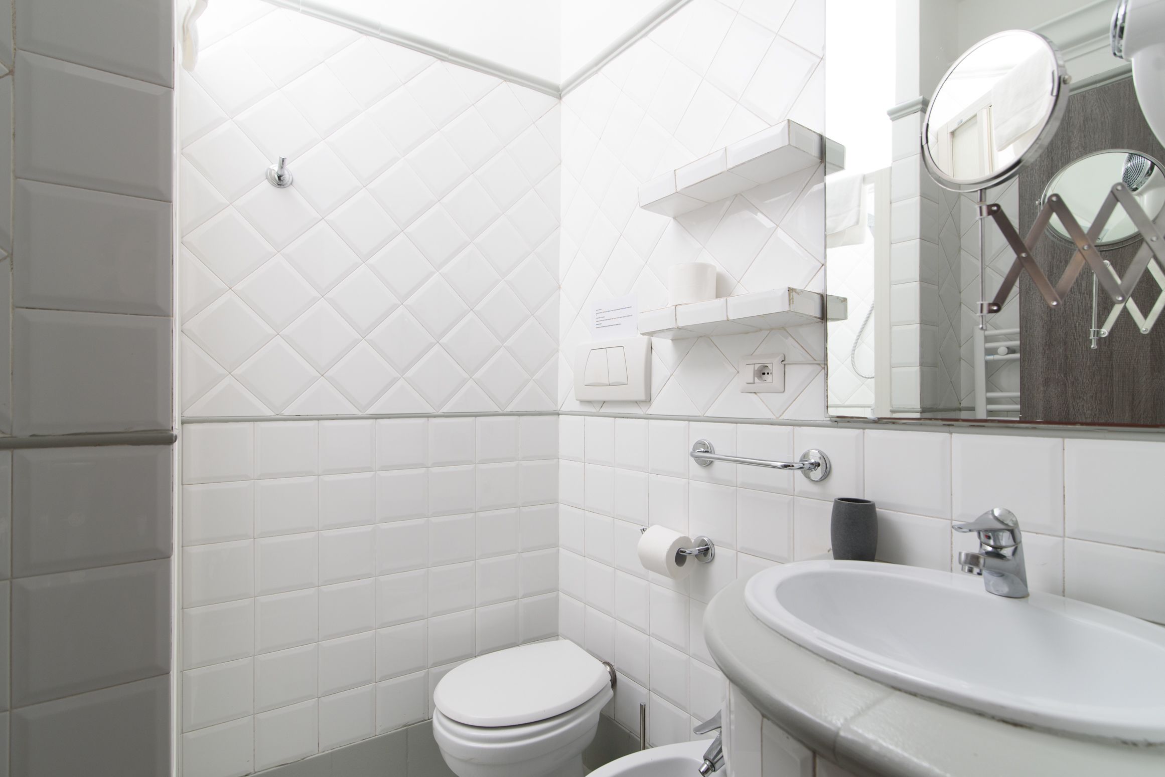 A modern bathroom with white tiled walls, a toilet, a sink, and a mirror.