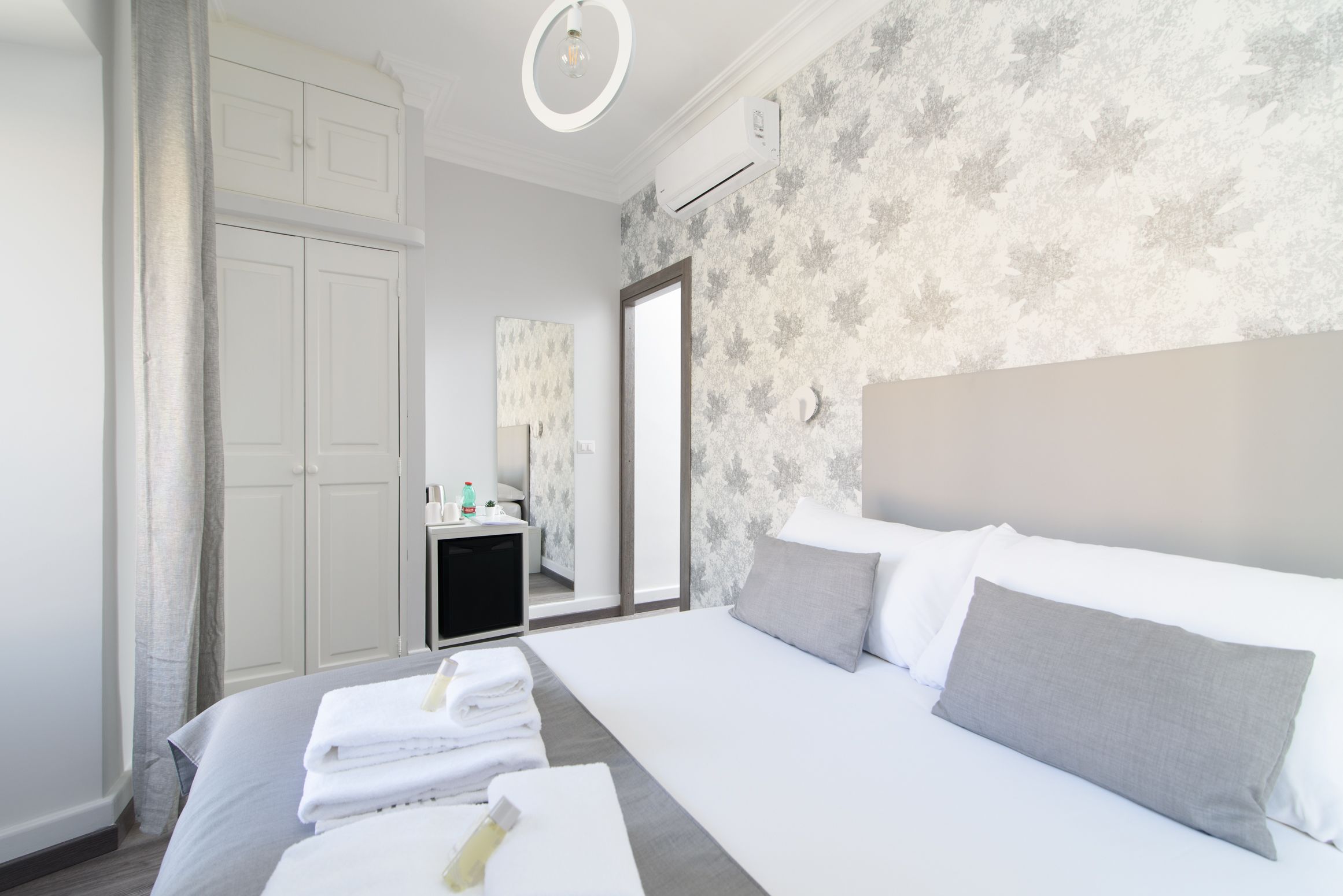 Moderni hotellihuone, jossa on suuri sänky, vaatekaappi, peilillä varustettu työpöytä ja kylpyhuone, joka näkyy oven läpi.