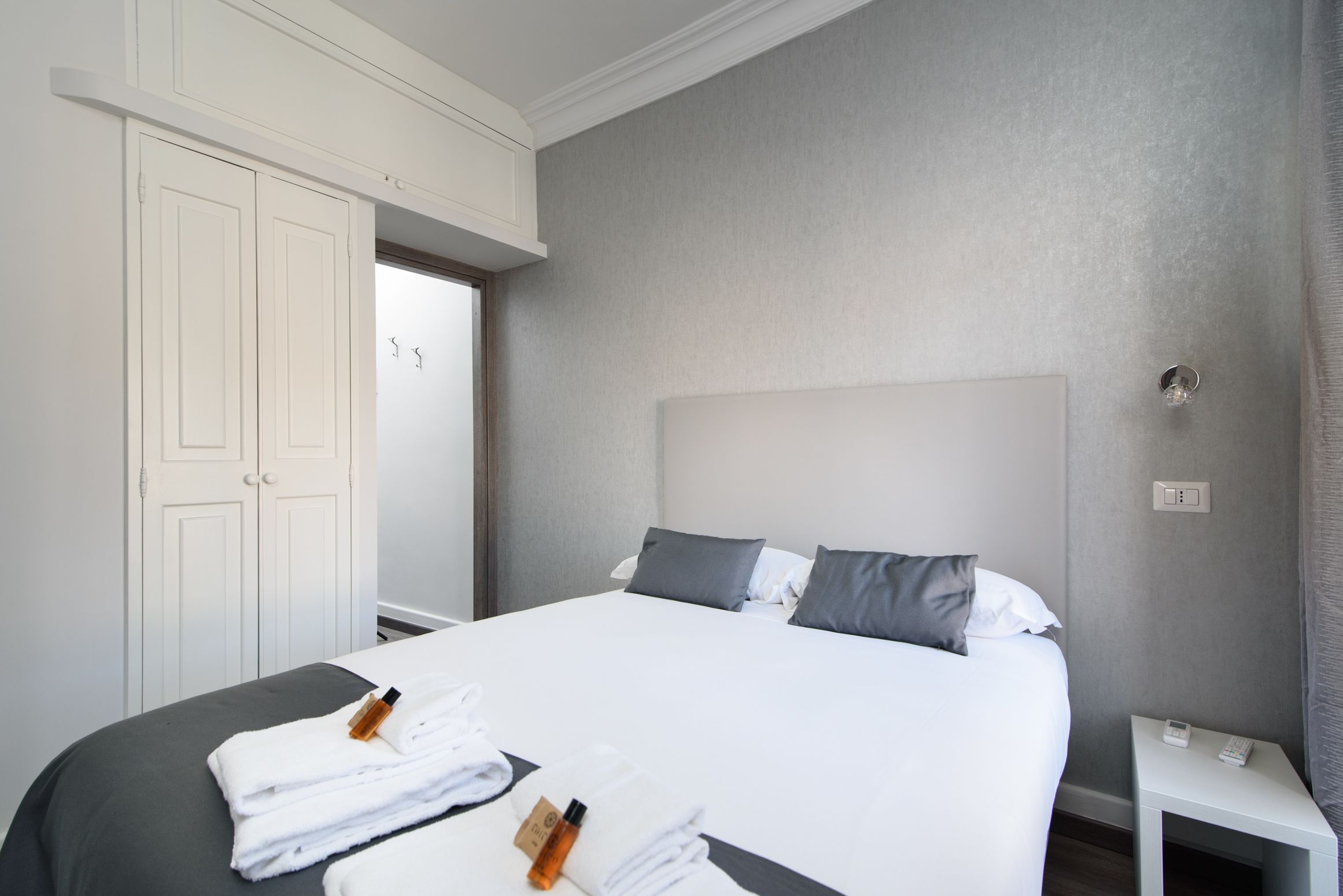 A hotel room with a large bed, white curtains, a bedside table with a phone, and a door leading to another room.