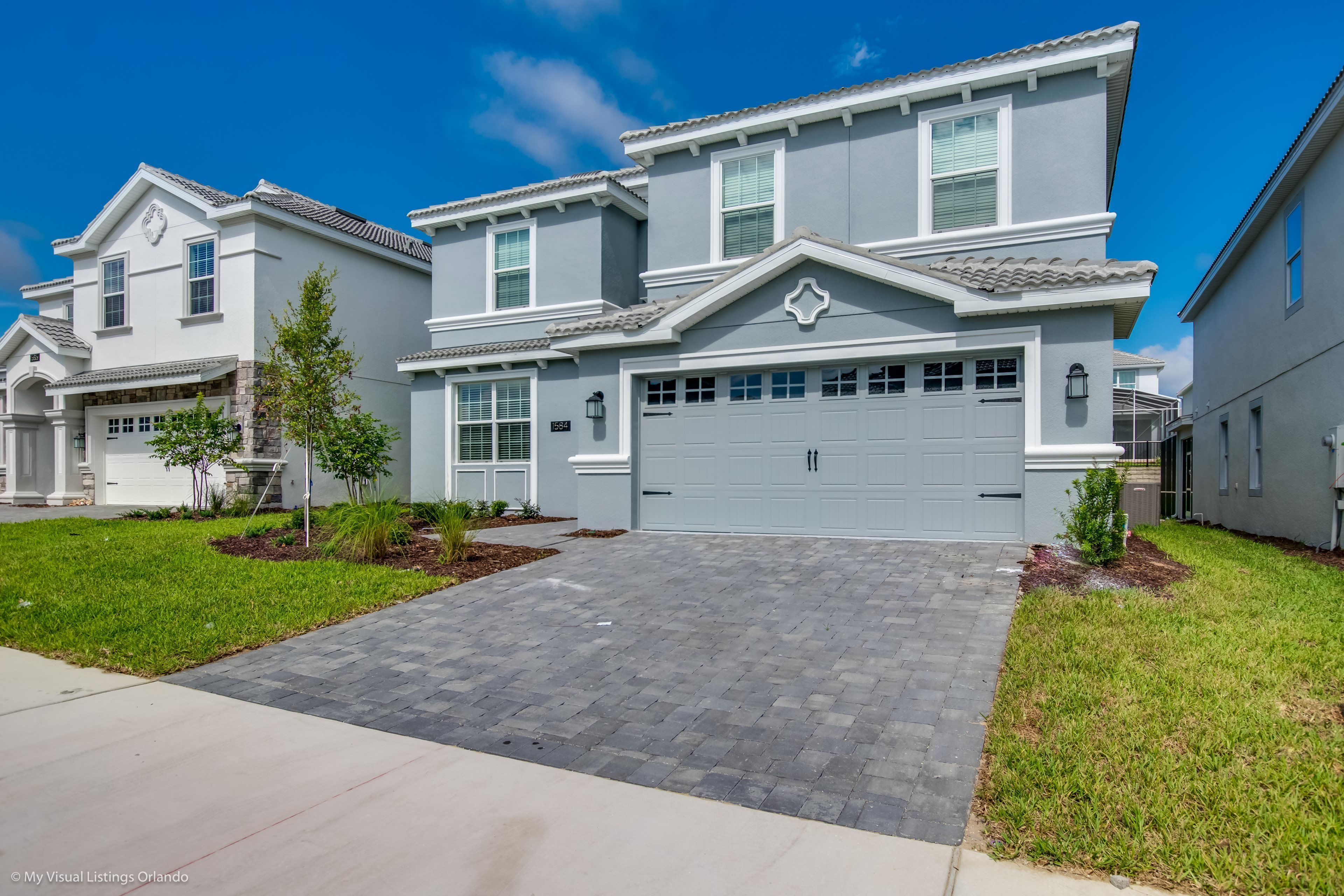 A two-story residential building with a grey facade, a central garage, and a paved driveway.