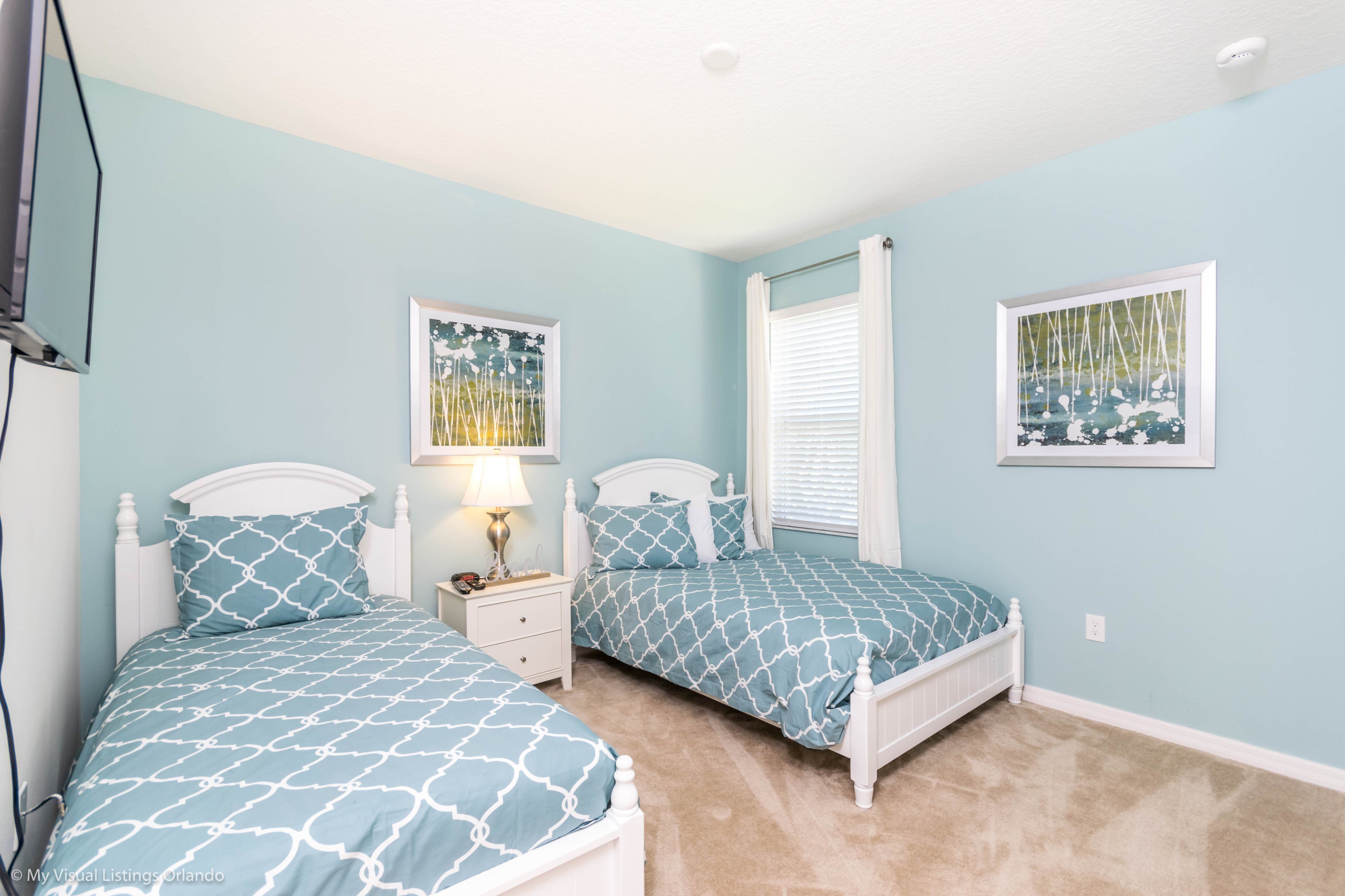 A bedroom with two beds, a nightstand, a lamp, and two framed pictures on the wall.