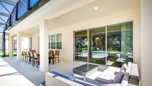 Patio moderno all'aperto con zona pranzo, posti a sedere e parete vetrata che si affaccia su una piscina.