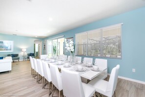 A dining area with a long table set for six, white chairs, and a vase of white flowers. - H6112 Beautiful 14 Bedroom 11 Bathroom Resoret (Davenport)