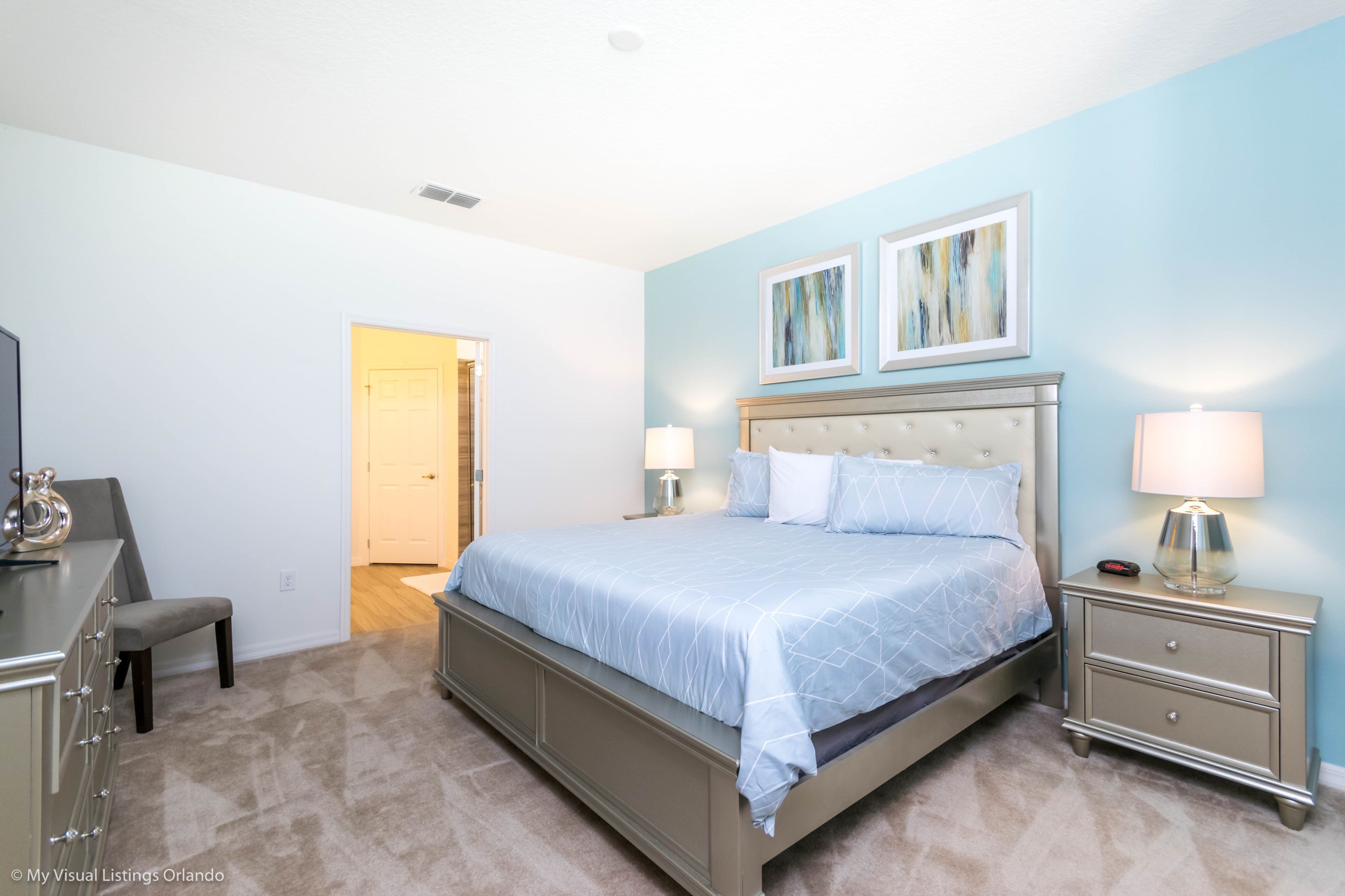 A bedroom with a bed, nightstands, a dresser, and artwork on the wall.