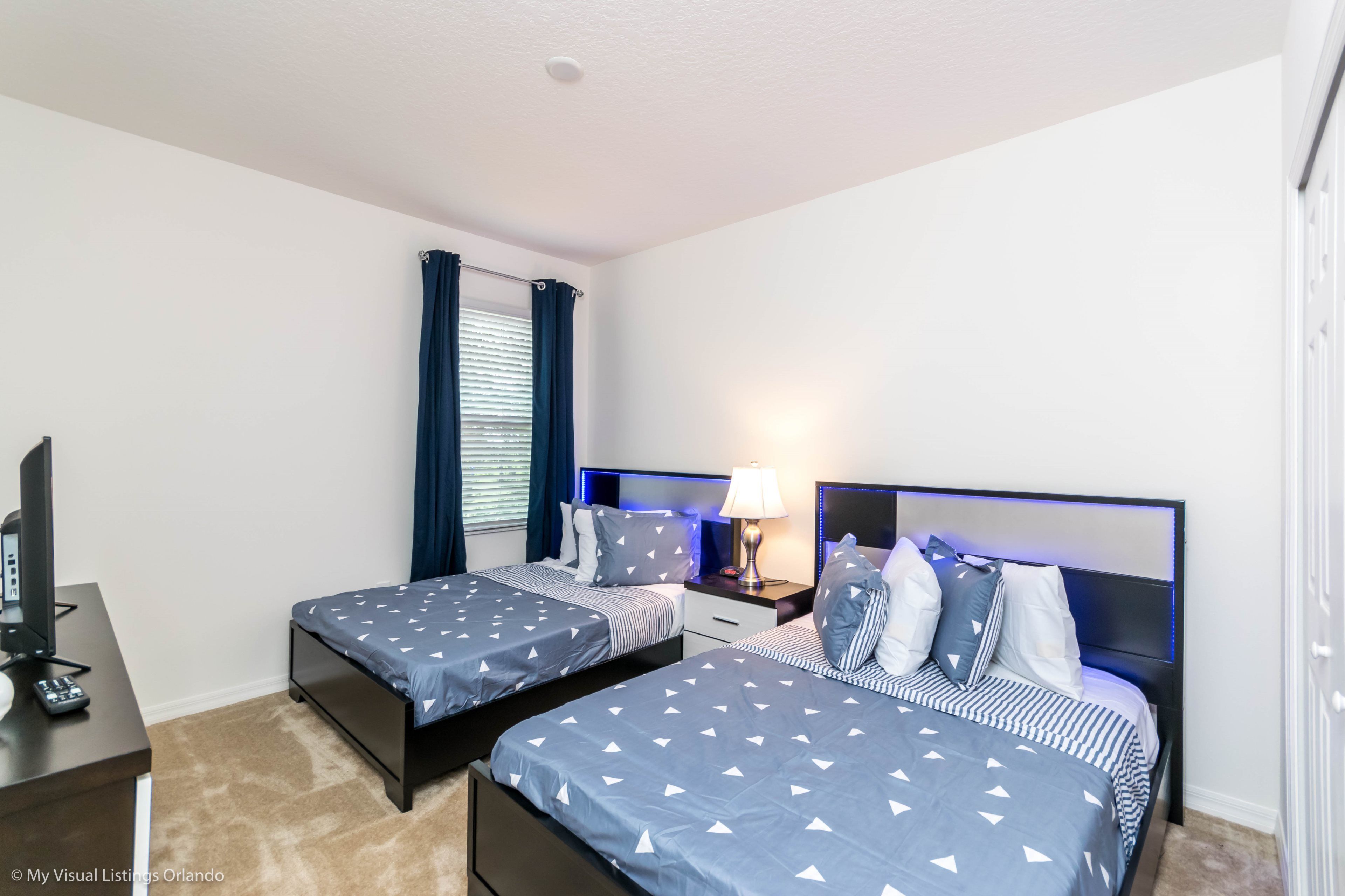 A hotel room with two beds, a desk with a computer, and a window with curtains.