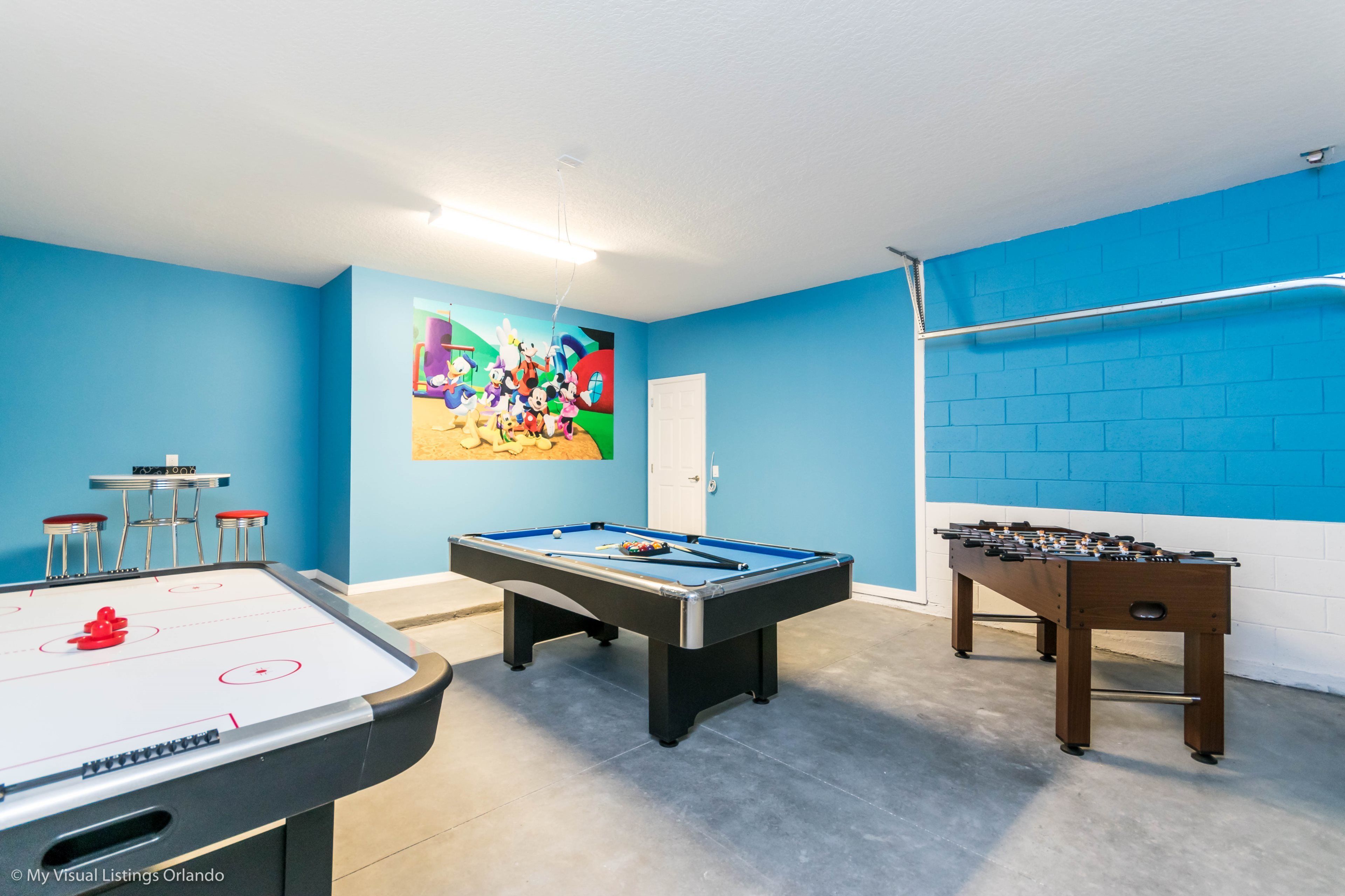 A room with a foosball table, a pool table, and a foosball table with a colorful mural on the wall.
