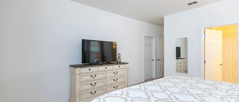 Une chambre à coucher avec un grand lit, une commode, un téléviseur et une porte donnant sur une autre pièce.