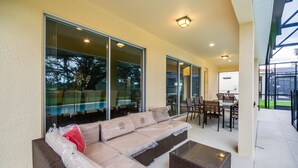 A covered patio area with a wicker sofa, a glass table, and a dining table with chairs. - H6108amazing Brand new 9 Bedroom 7 Bathroom Resort (Davenport)