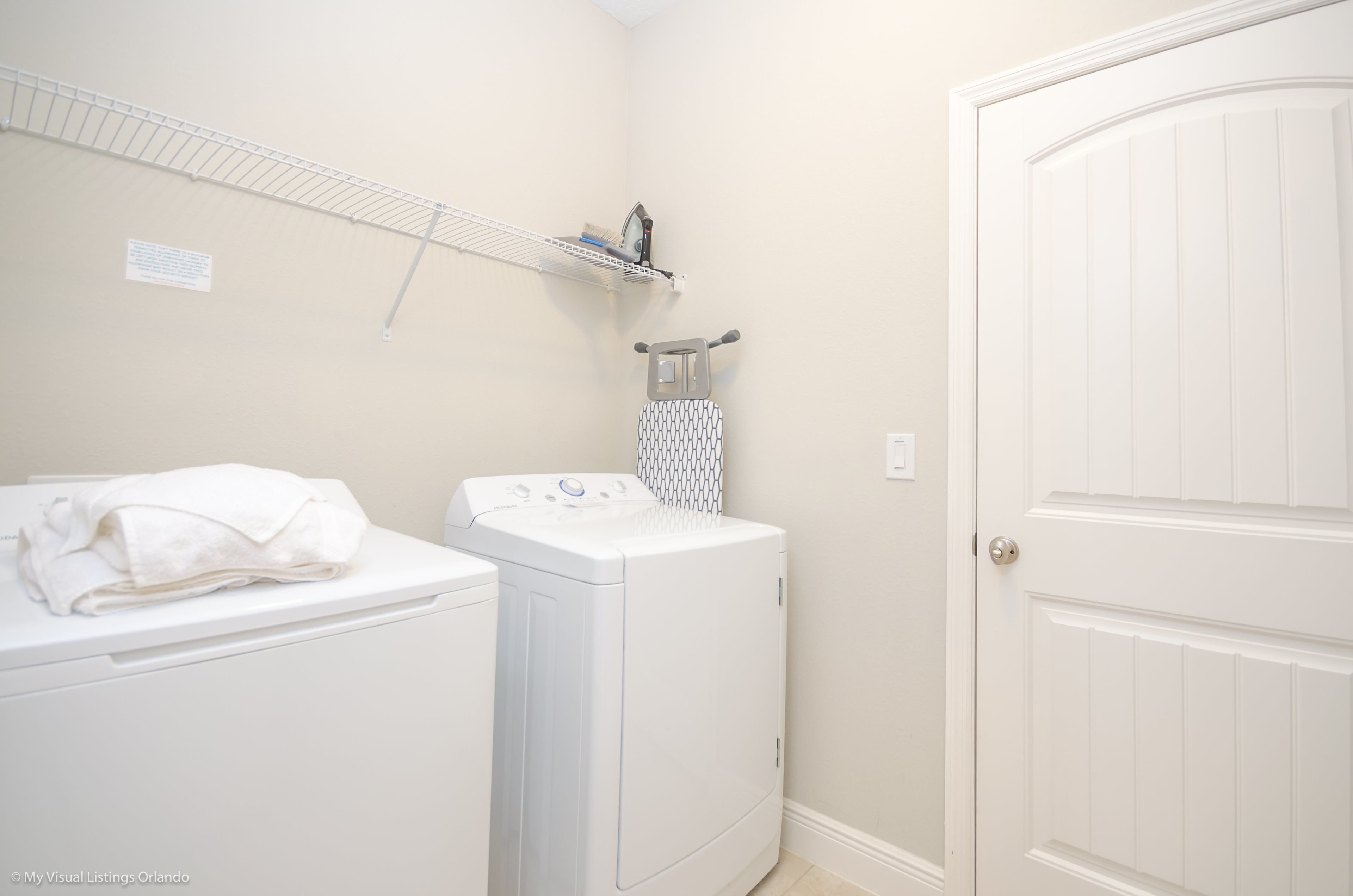 A laundry area with a washing machine and dryer, a drying rack, and a door.