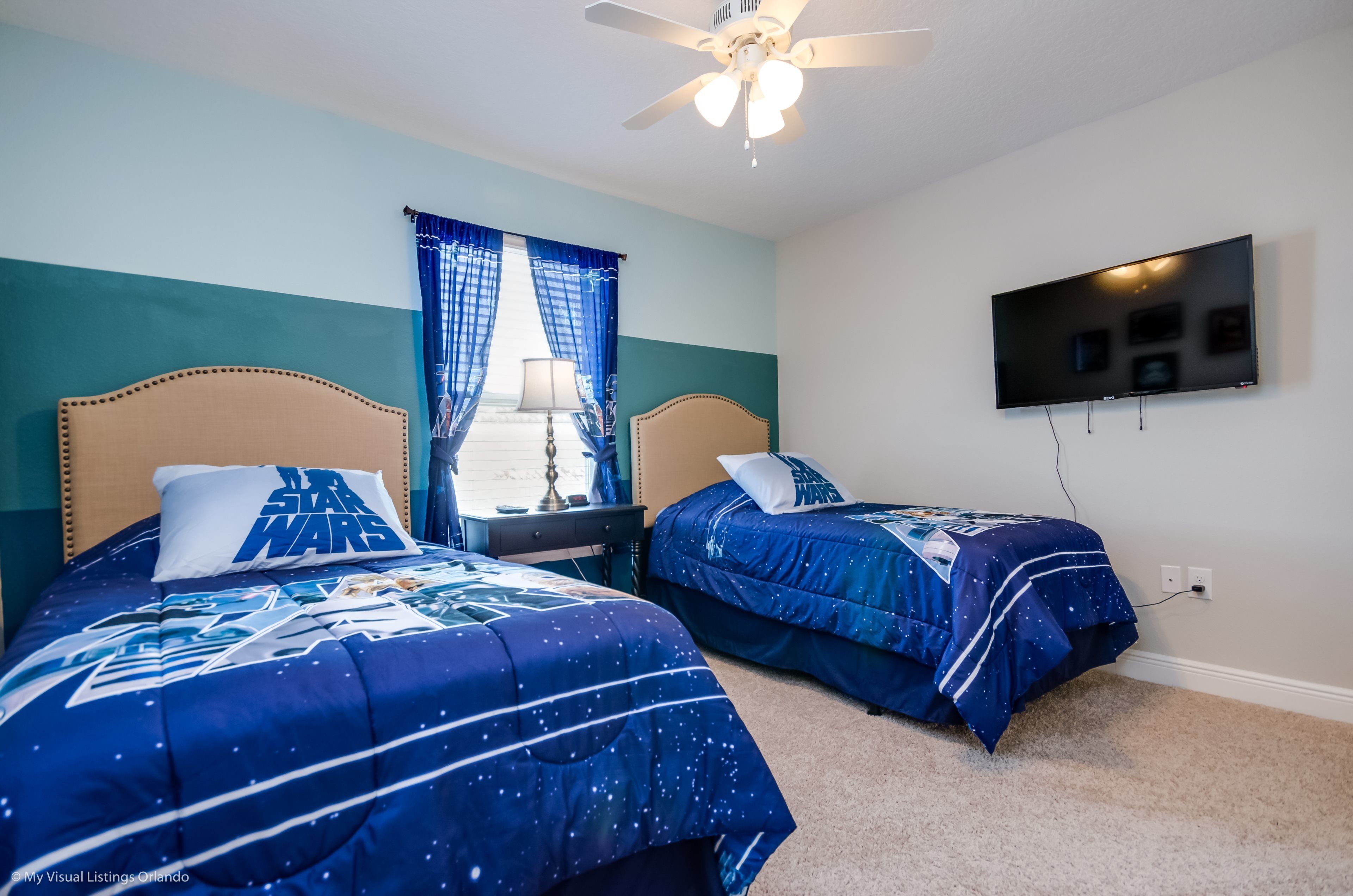 A bedroom with two beds, a ceiling fan, a TV, and a window with curtains.