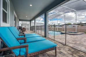 Uma área externa coberta com espreguiçadeiras e piscina.