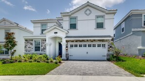 A two-story house with a white facade, a stone accent wall, a garage, and a well-maintained front yard.