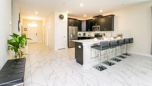 A modern kitchen with dark cabinets, a central island with bar stools, and a clock on the wall.