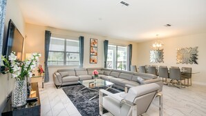 A modern living room with a sectional sofa, a glass coffee table, and a dining area with a chandelier.