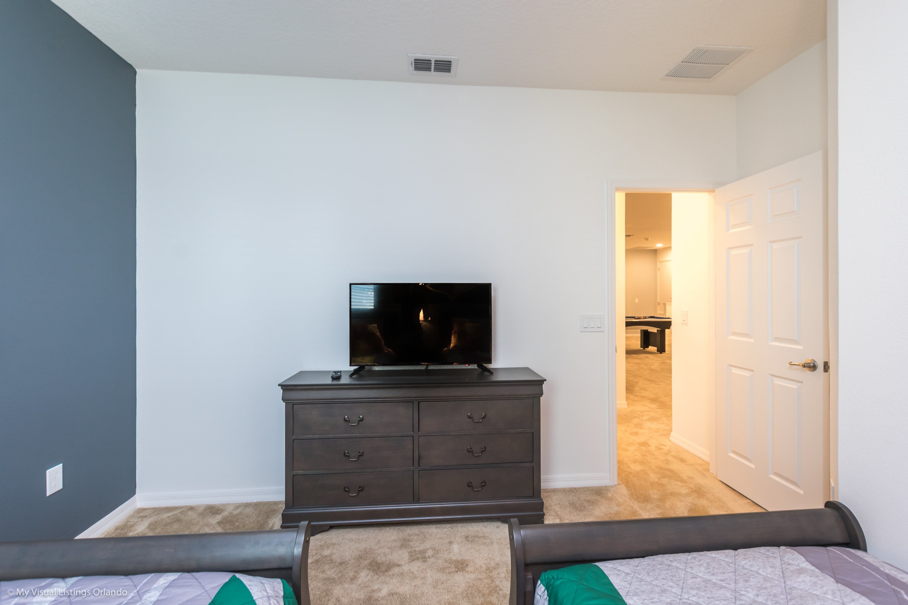 A bedroom with a dark dresser, a flat-screen TV, and a bed with a green pillow.