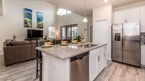 A modern kitchen with a central island, stainless steel appliances, and a dining area with a sofa and TV. - H5424 Ultimate 5 Bedroom 5 Bathroom Luxury Villa (Davenport)