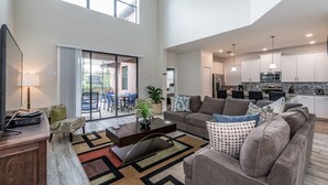 A spacious living area with a sofa, coffee table, and a TV. There is a sliding glass door leading to an outdoor patio. - H5424 Ultimate 5 Bedroom 5 Bathroom Luxury Villa (Davenport)