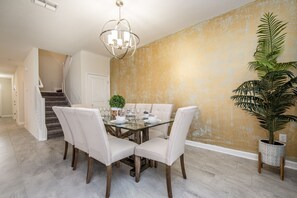 A dining area with a glass table, white upholstered chairs, a chandelier, a staircase, and a large potted plant. - H1675 Brand new Luxury 8 Bedroom 5 Bathroom Villa (Davenport)