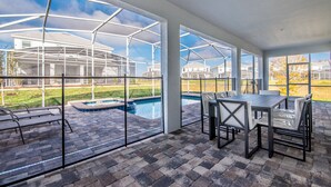 Une terrasse couverte avec une piscine, des sièges d’extérieur et de grandes fenêtres offrant une vue sur le quartier.